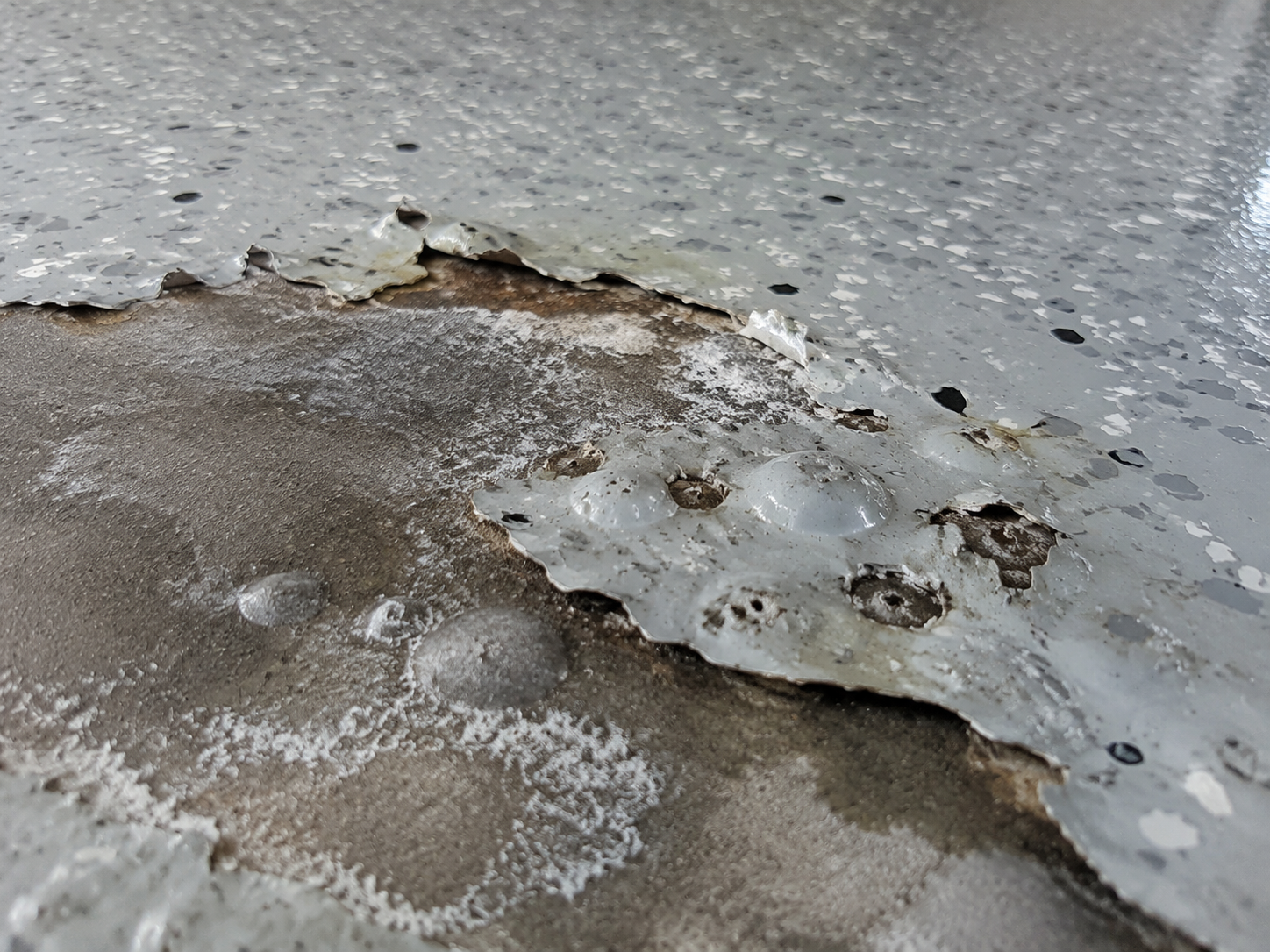 Epoxy floor coating peeling and bubbling from moisture-damaged concrete.