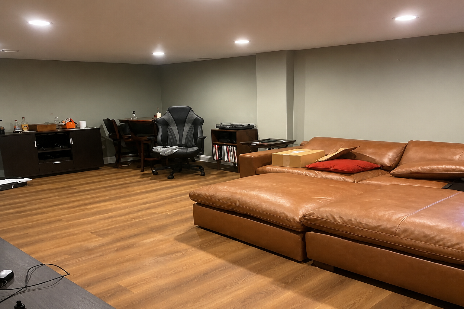 Furnished room with freshly painted gray walls, recessed lighting, wood flooring, and a brown sectional sofa.