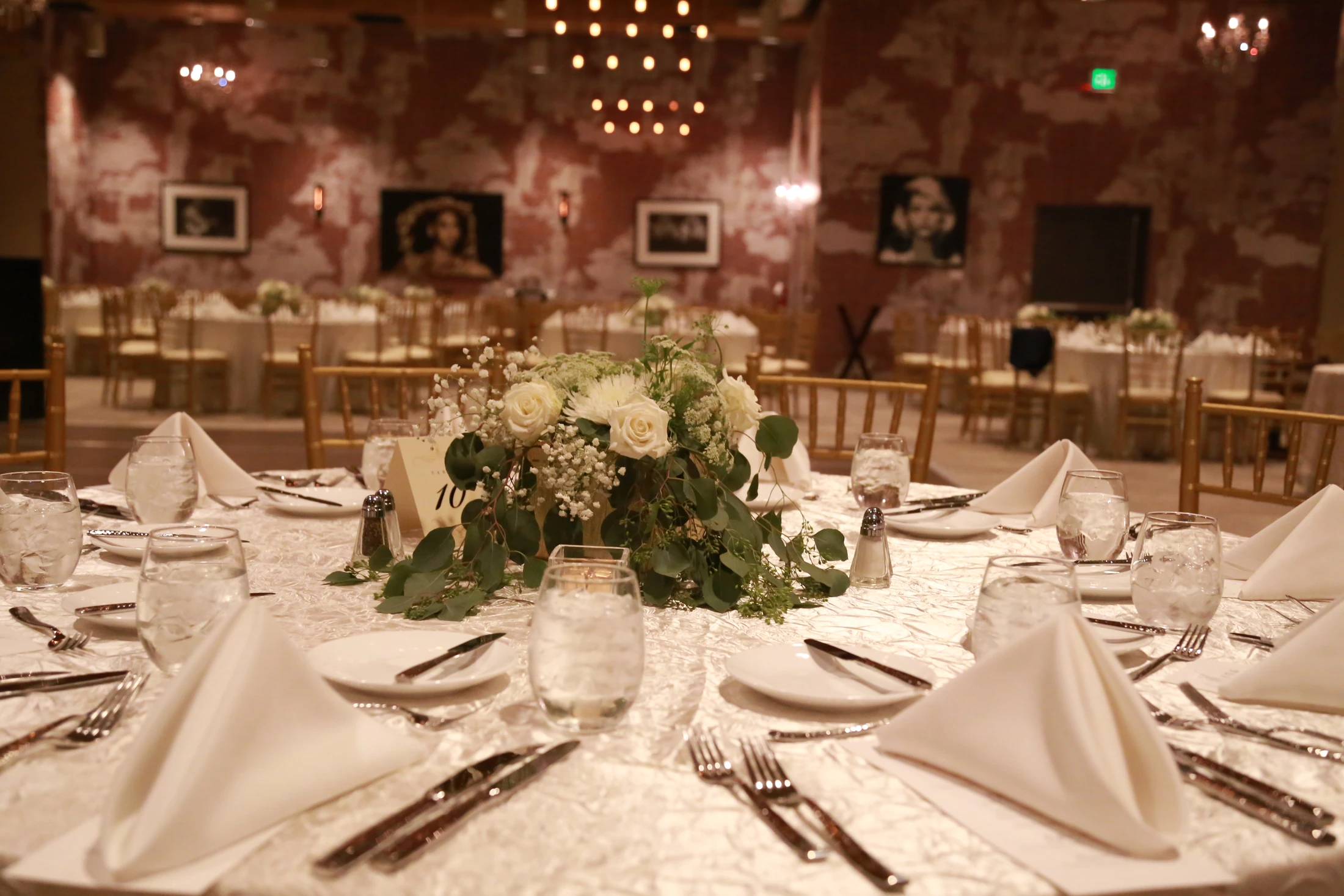 Floral centerpieces and gold chairs at a Whitney Peak wedding reception, with the room and chandeliers beyond