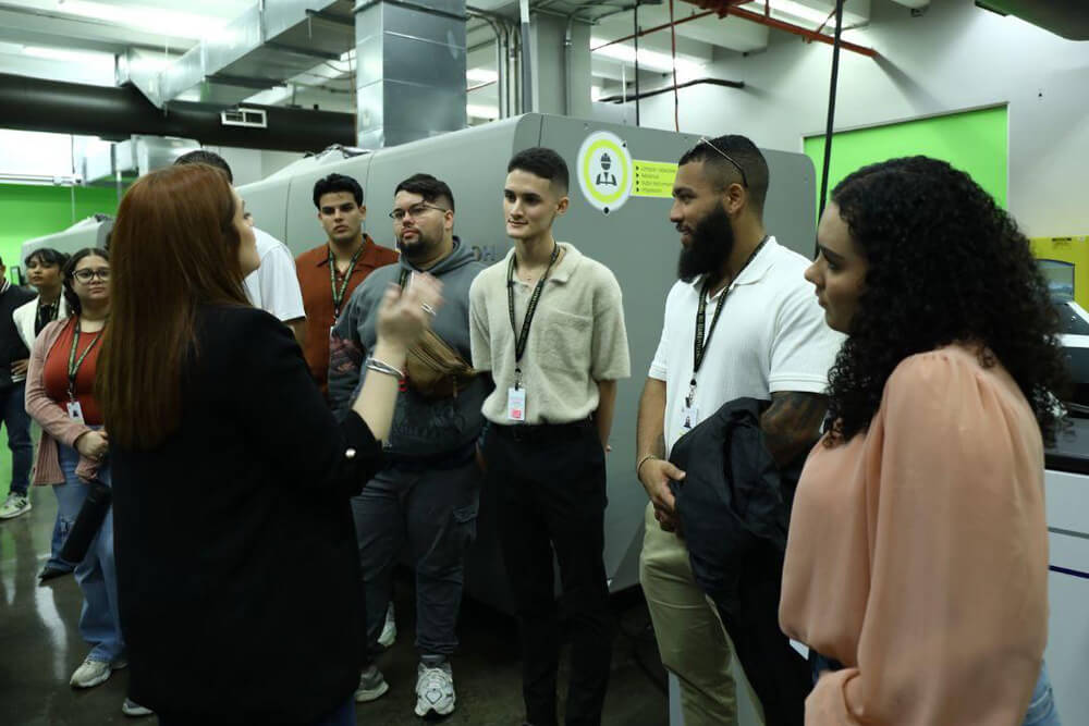 Grupo de personas jóvenes y profesionales en una reunión, sonriendo y colaborando mientras observan una tableta digital. La escena refleja un ambiente laboral positivo y dinámico.