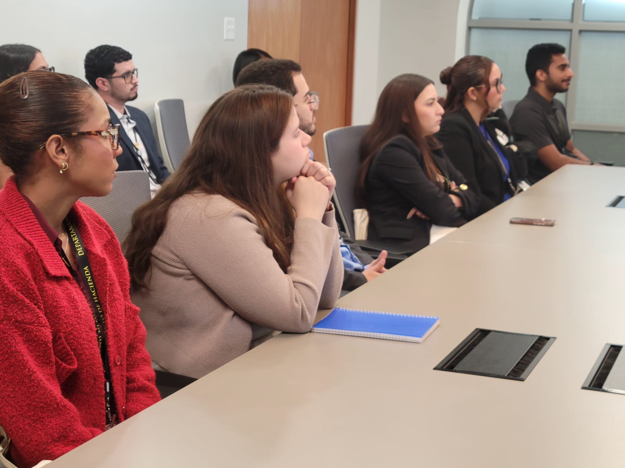 Grupo de personas jóvenes y profesionales en una reunión, sonriendo y colaborando mientras observan una tableta digital. La escena refleja un ambiente laboral positivo y dinámico.