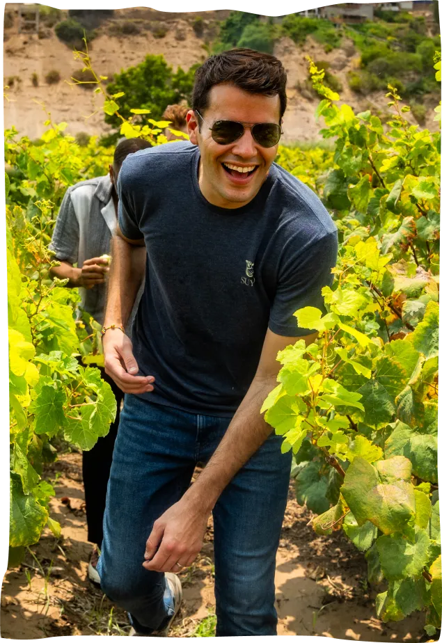 A man standing in a field with a bottle of wine.