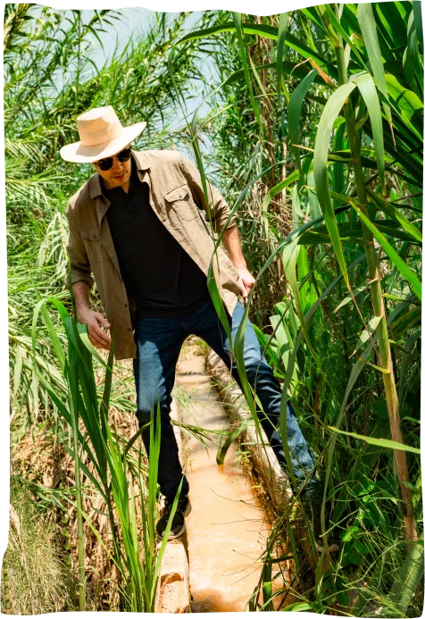 A man in a hat and sunglasses walking across a bridge.
