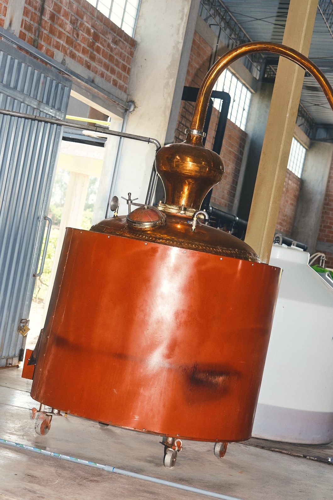 Copper distillation with curved top pipe on wheels inside distillery.