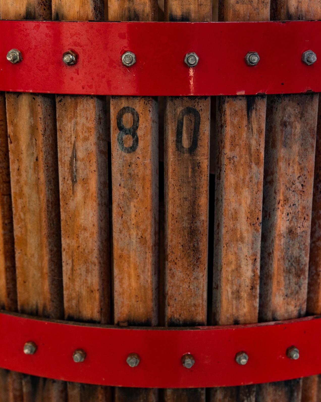 Close-up of a grape press with wooden slats and red metal bands, showing numbers 8 and 0.