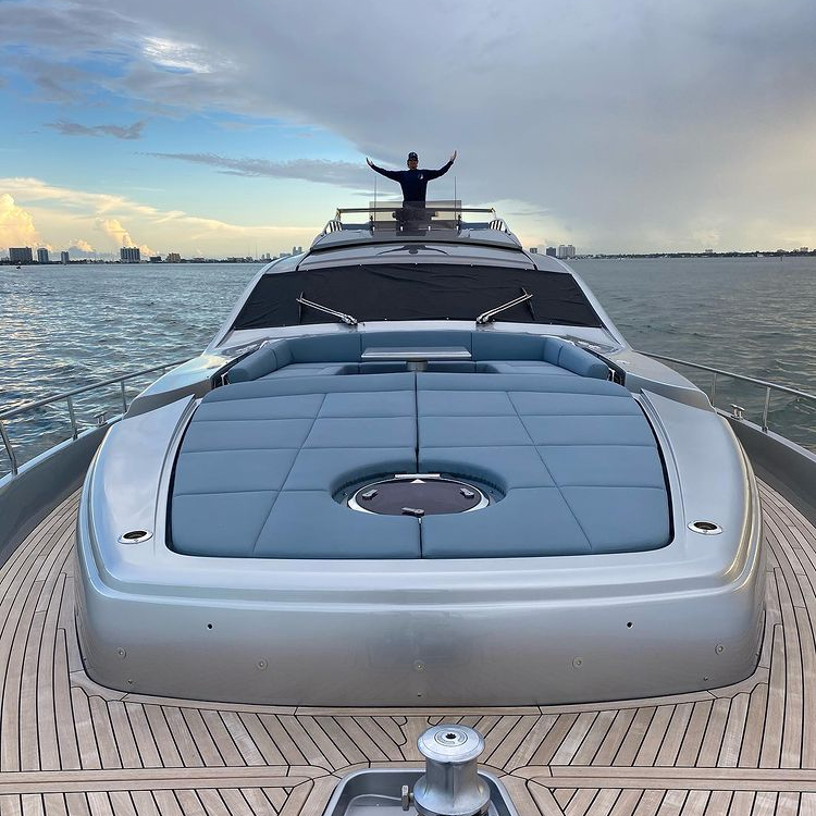 Miami Yachting crew member standing on the bow of a luxury yacht in Miami, arms raised, with the skyline in the background.