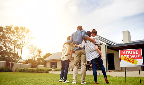 Family of four embracing while looking at their new home with a sold sign on the lawn.