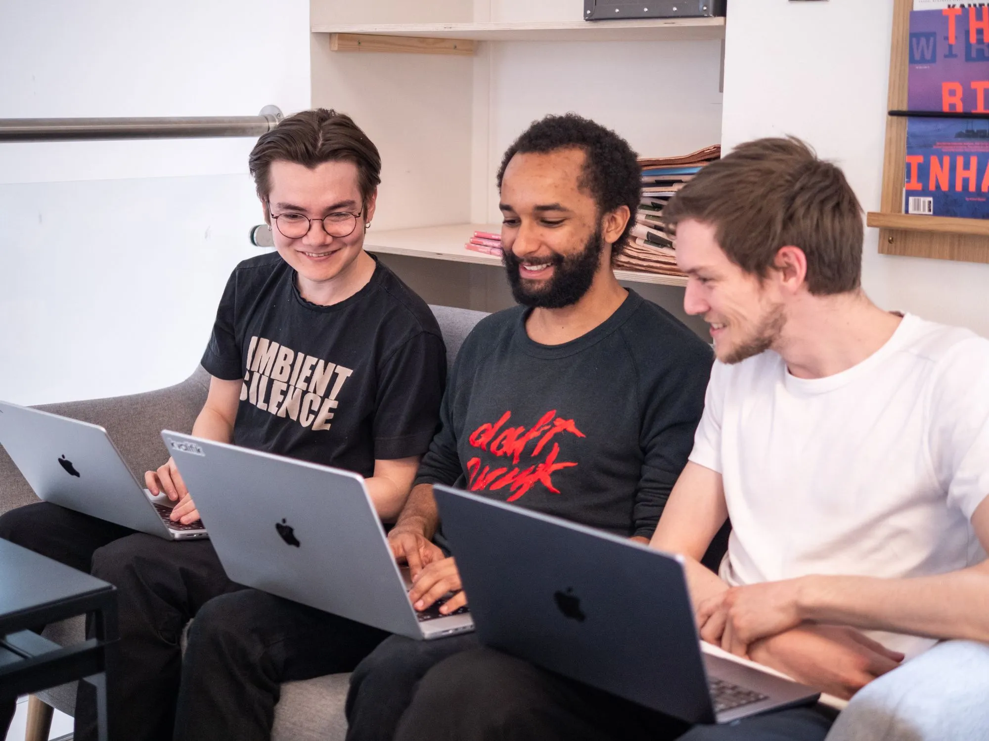 Three smiling colleagues working on laptops together on a couch.