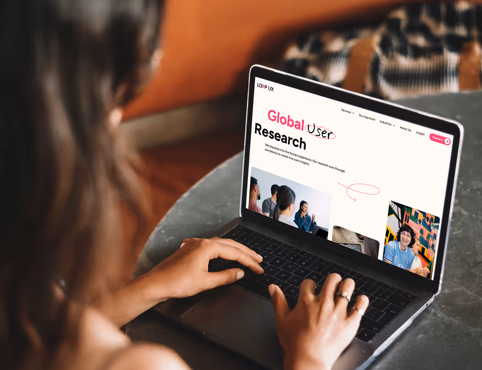 Person typing on a laptop showing a webpage titled 'Global User Research' with images of people in a meeting.