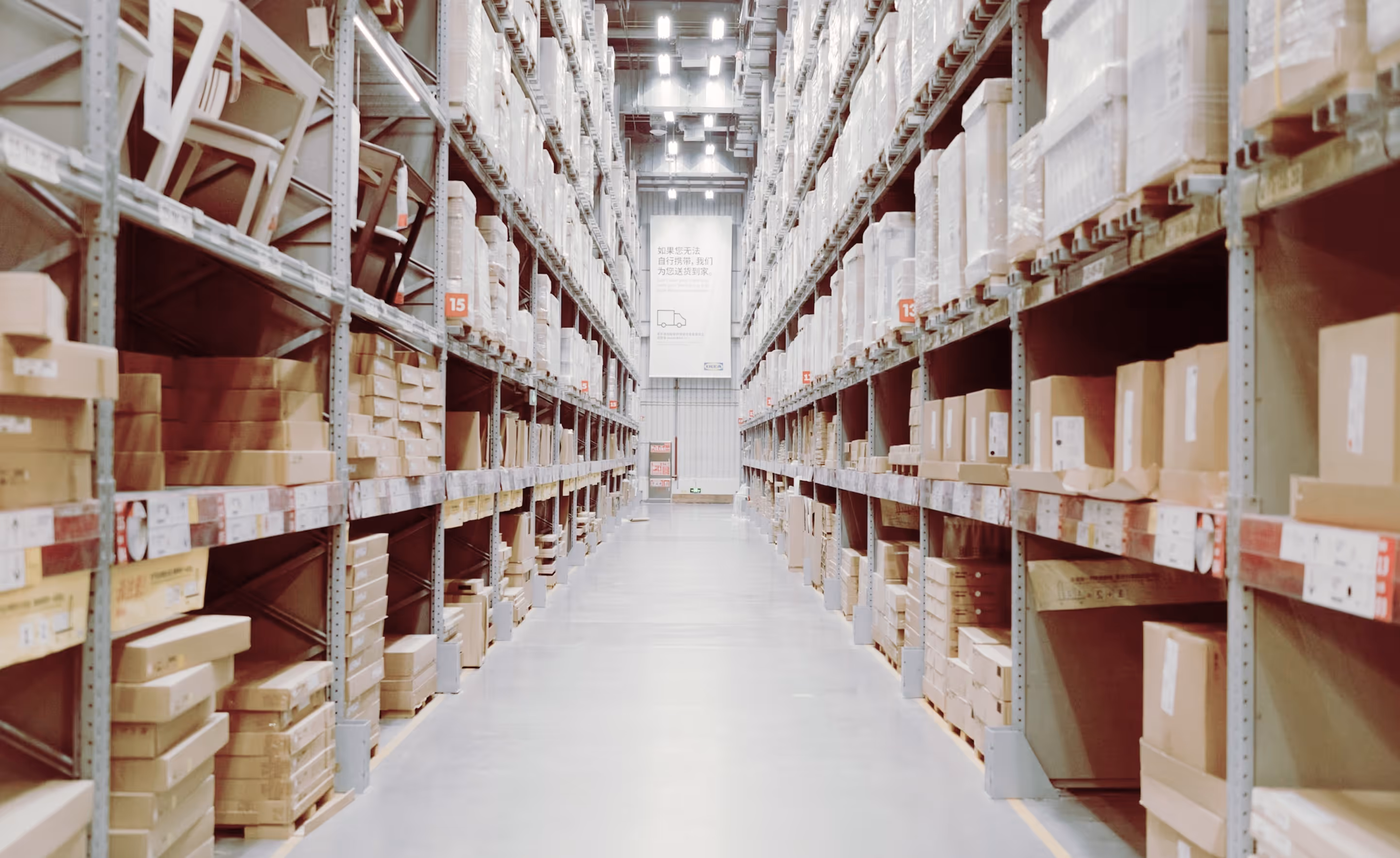 Long aisle in a warehouse with tall shelves stacked with boxes and flat-pack furniture.
