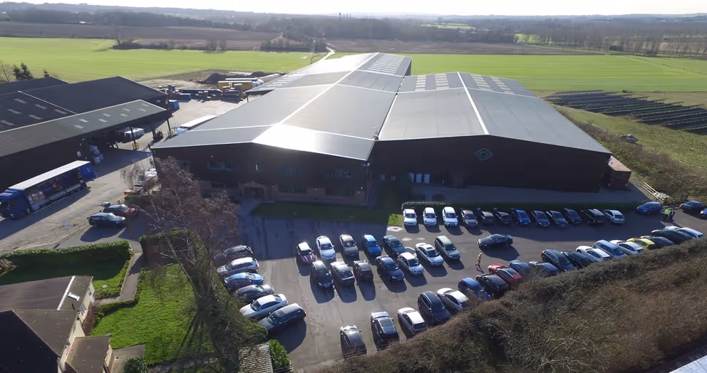 A large warehouse surrounded by numerous parked cars and green fields.