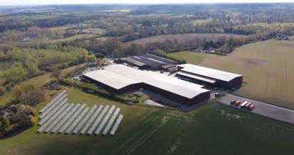 Aerial view of a large industrial facility with solar panels installed on adjacent grassy fields.