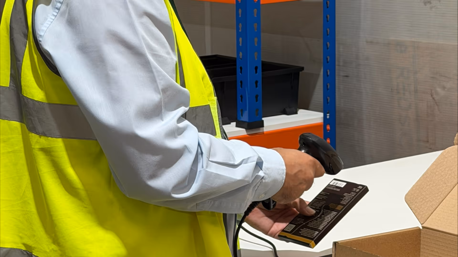 A person in a yellow vest scans a package with a barcode scanner.