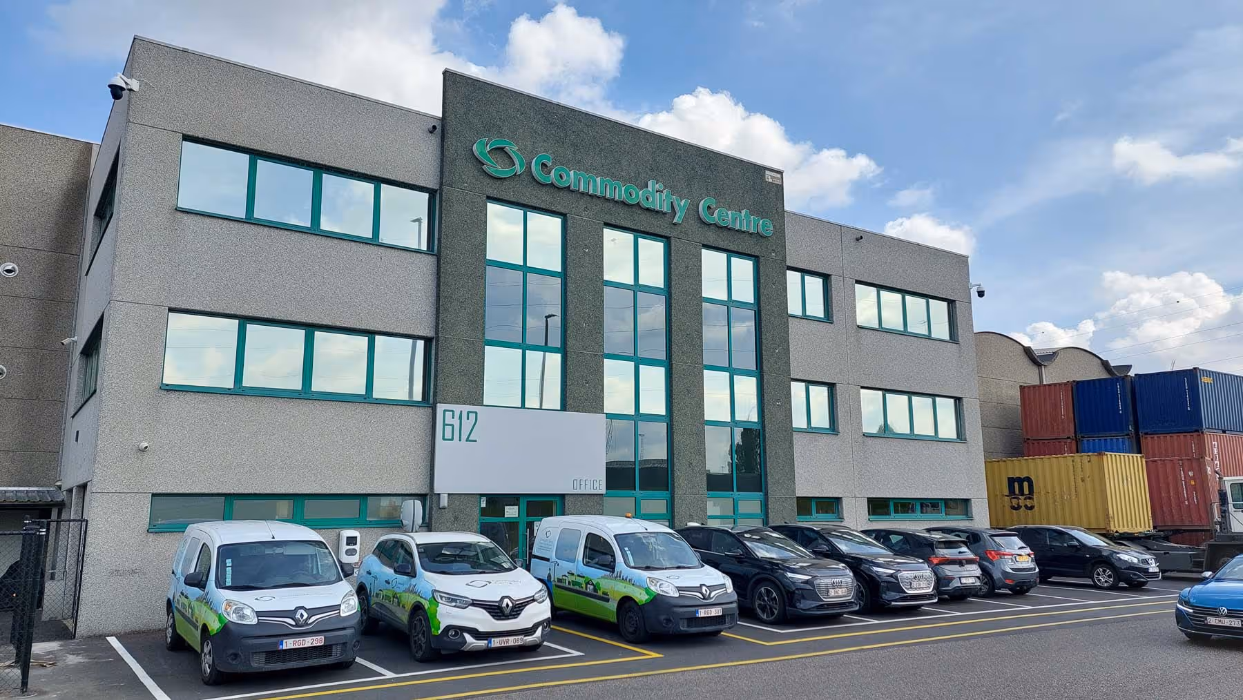 Immeuble de bureaux de trois étages avec un panneau vert « Commodity Center » et des voitures garées devant.