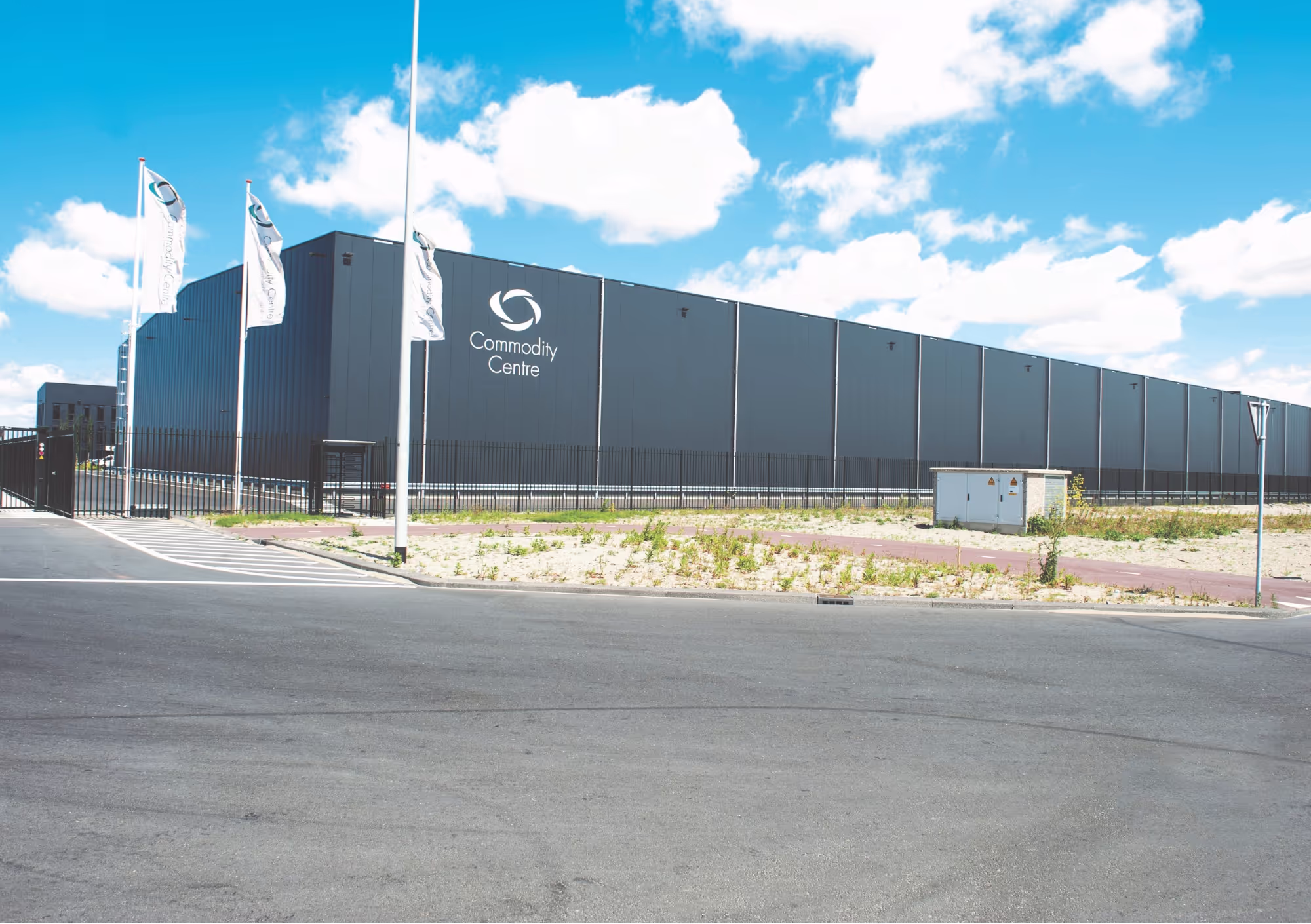 Large industrial building labeled "Commodity Centre" with flags and a surrounding fence under a blue sky.