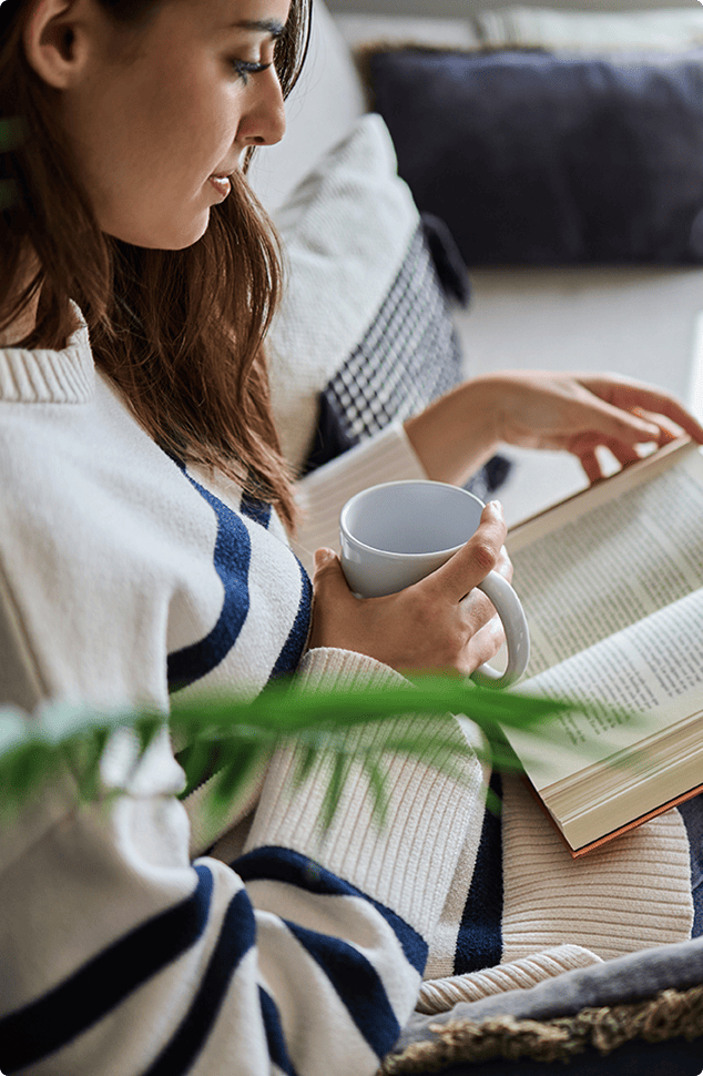 A serene setting with a lady reading a book and drinking coffee on the sofa