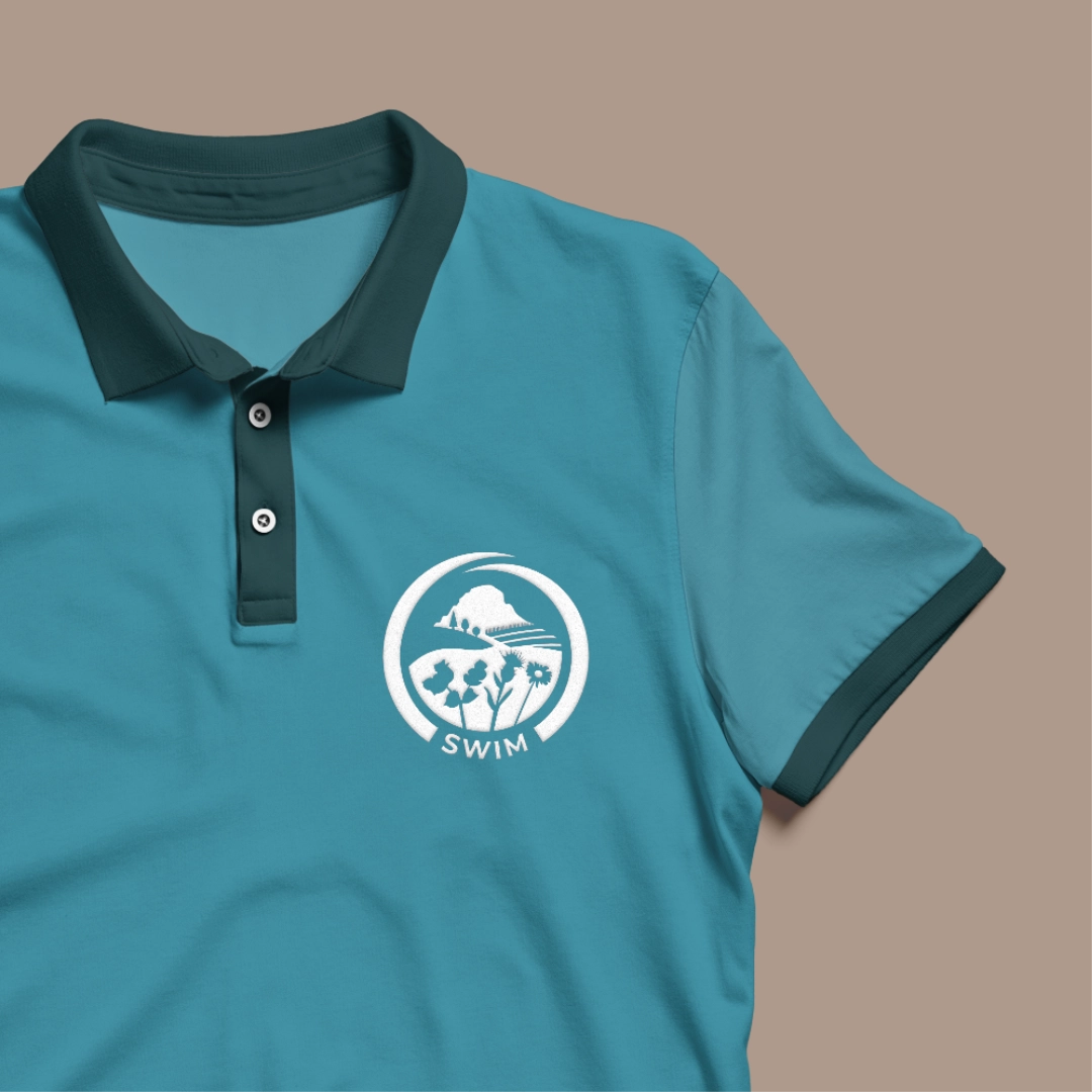 SWIM logo, flat illustration of invasive plants in-front of lowlands and a mountain, on a t-shirt.