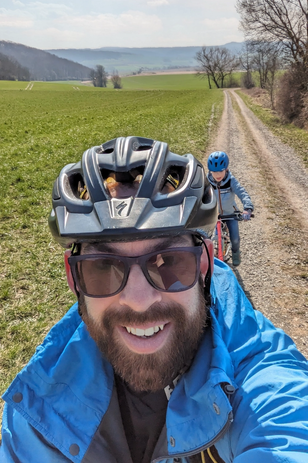 Selfie while cycling up a dirt track in the countryside on a sunny day. I'm towing my son using a bungee chord and have a big smile on my face.