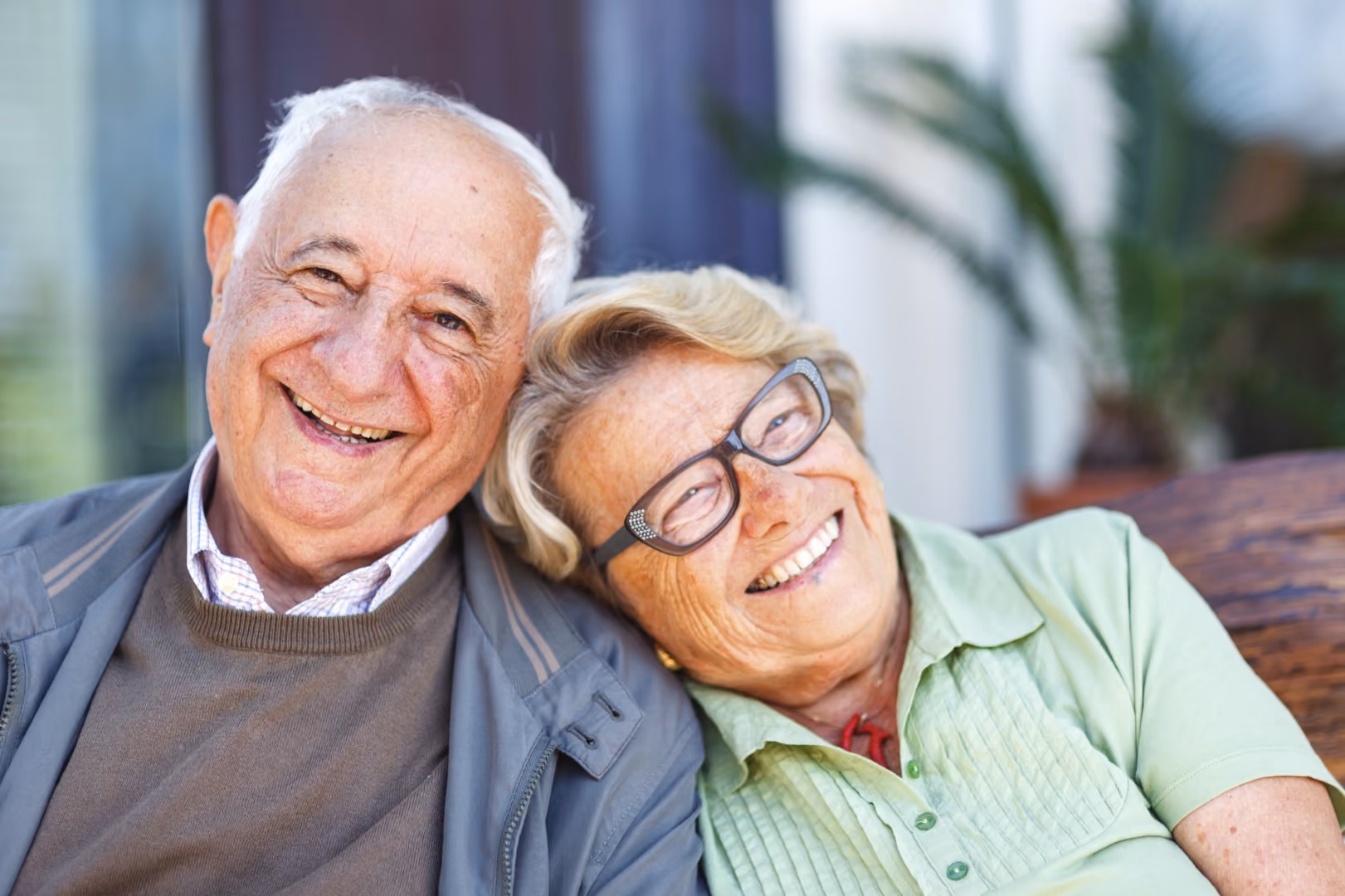 Happy elderly couple smiling close together on a bench outdoors.