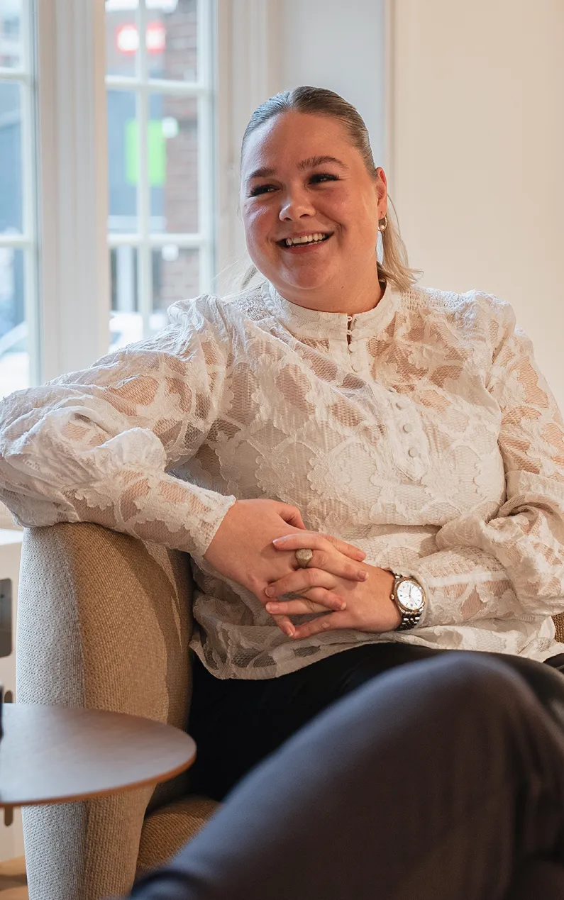 En kvinde sidder på en sofa og smiler til kameraet.
