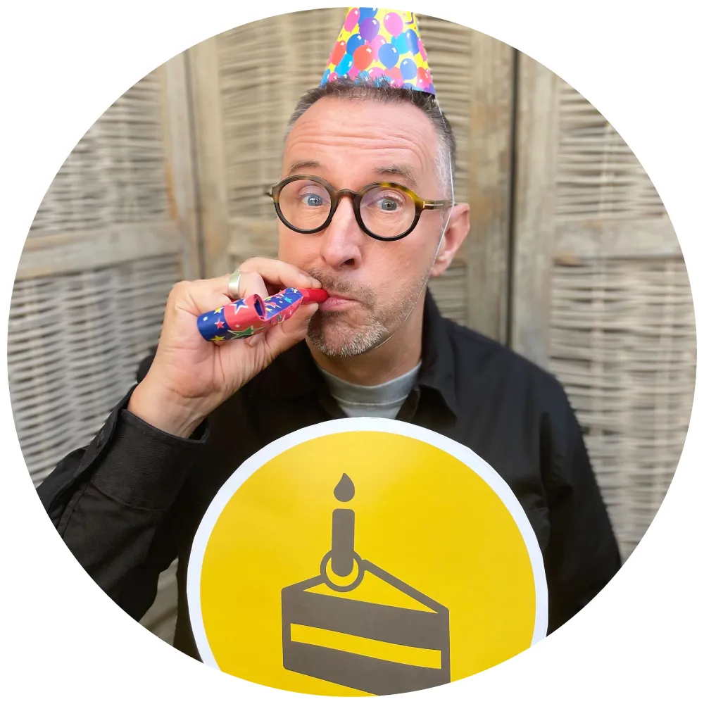 Host Chris Grimes in party hat blowing noisemaker whilst holding the Big Birthday Show icon