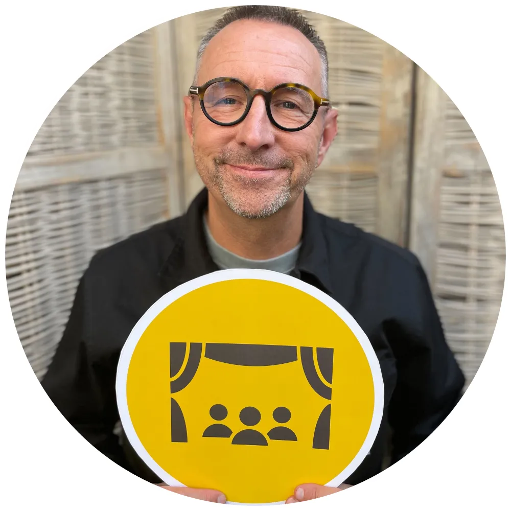Podcast host - Chris Grimes - holding yellow sign with a live theatre audience icon