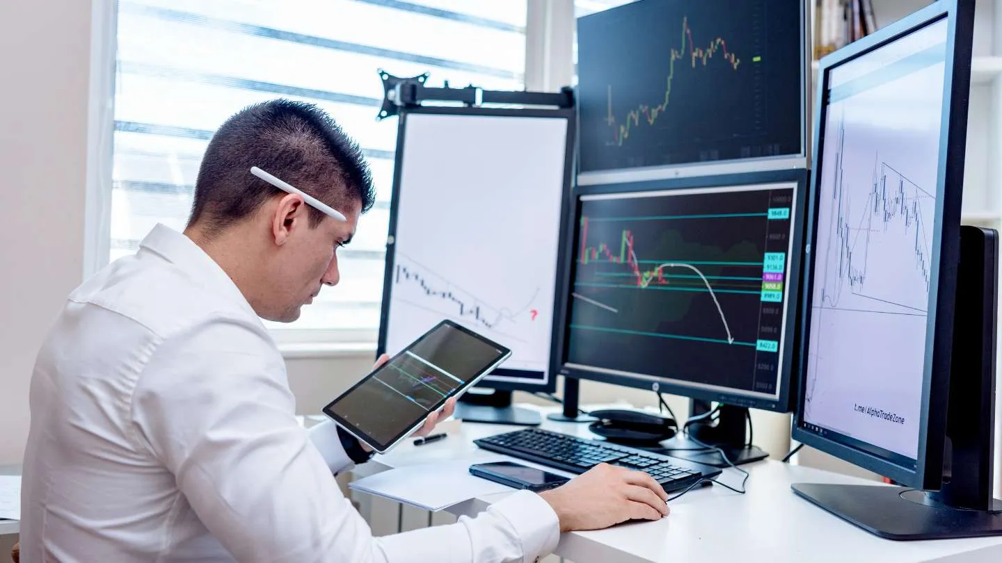 Man in white shirt analyzing stock market charts on multiple monitors and a tablet in a bright office, streamlinead communication