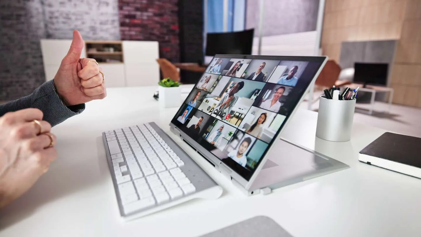 Person showing thumbs up next to a keyboard in front of a tablet displaying a group video call with multiple people.