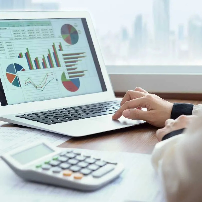 Person working on a laptop displaying various colorful charts and graphs with a calculator on the desk.