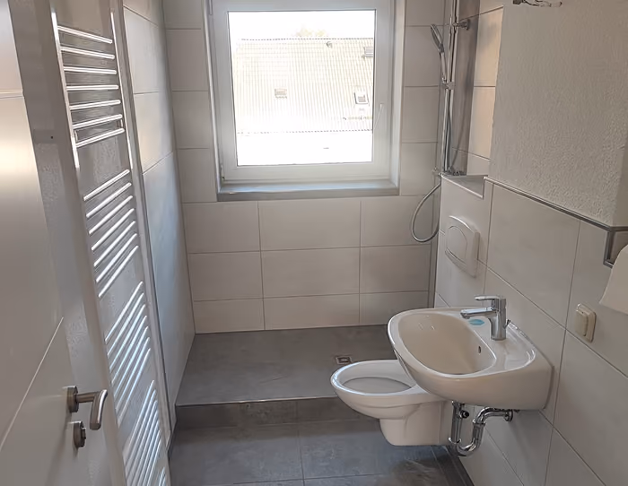 Kleines Badezimmer mit Toilette, Waschbecken, Handtuchheizung und Fenster über der Duschfläche.