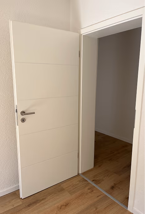 Weiße Innentür geöffnet zu einem Raum mit Holzboden und weißen Wänden.