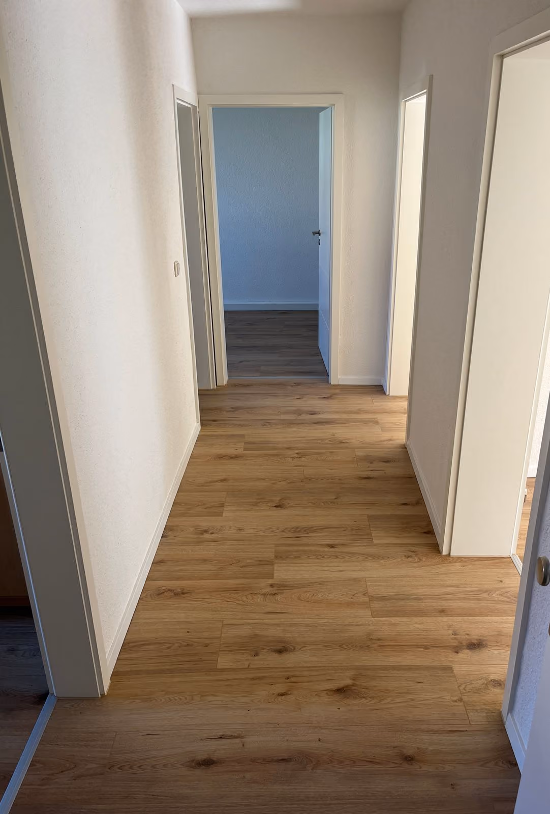 Flur mit hellem Holzboden und weißen Wänden, mit mehreren offenen weißen Türen.