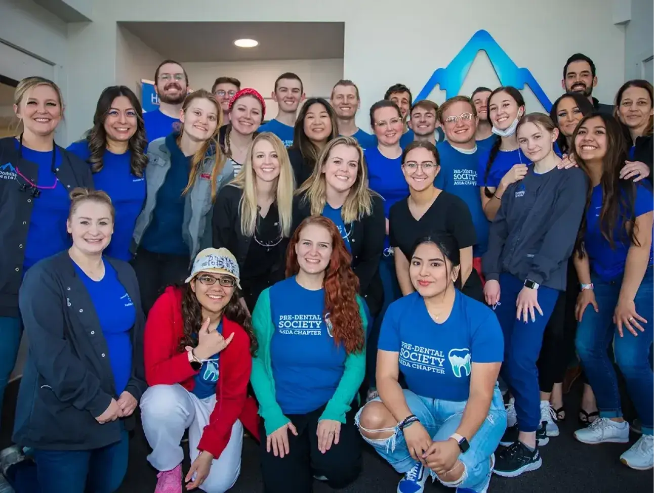 A group of people wearing matching shirts poses together in a room, smiling at the camera.