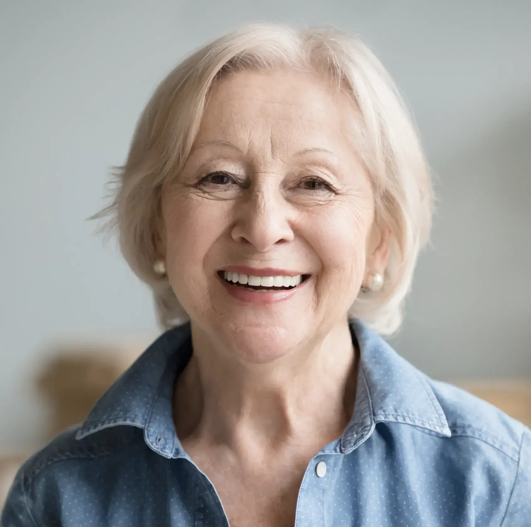 Smiling older woman with short gray hair, wearing a blue button-up shirt.