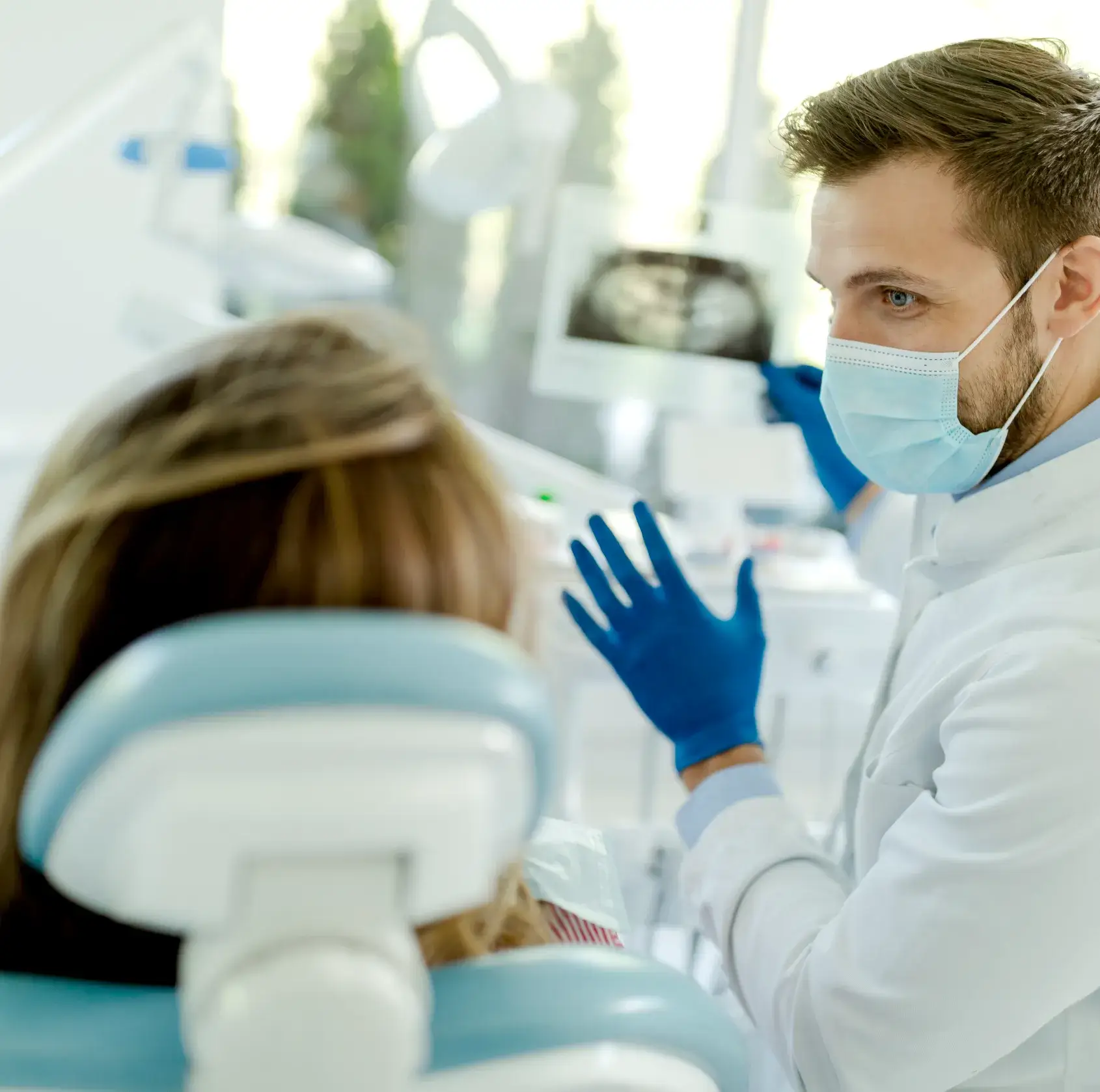 Dentist discussing an X-ray with a patient in a dental chair, both wearing protective masks.