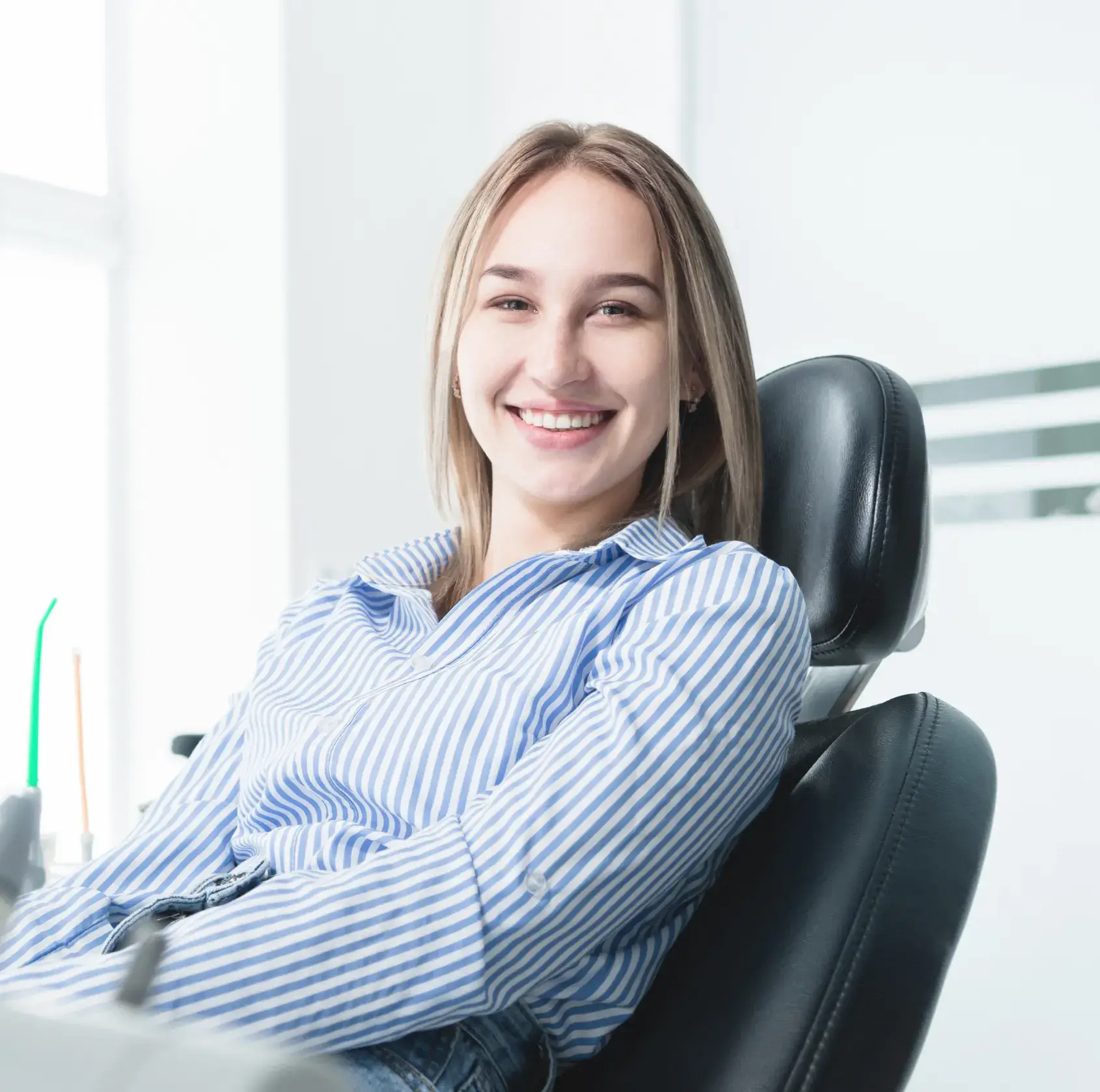 A woman in a striped shirt smiles while sitting in a dentist's chair.