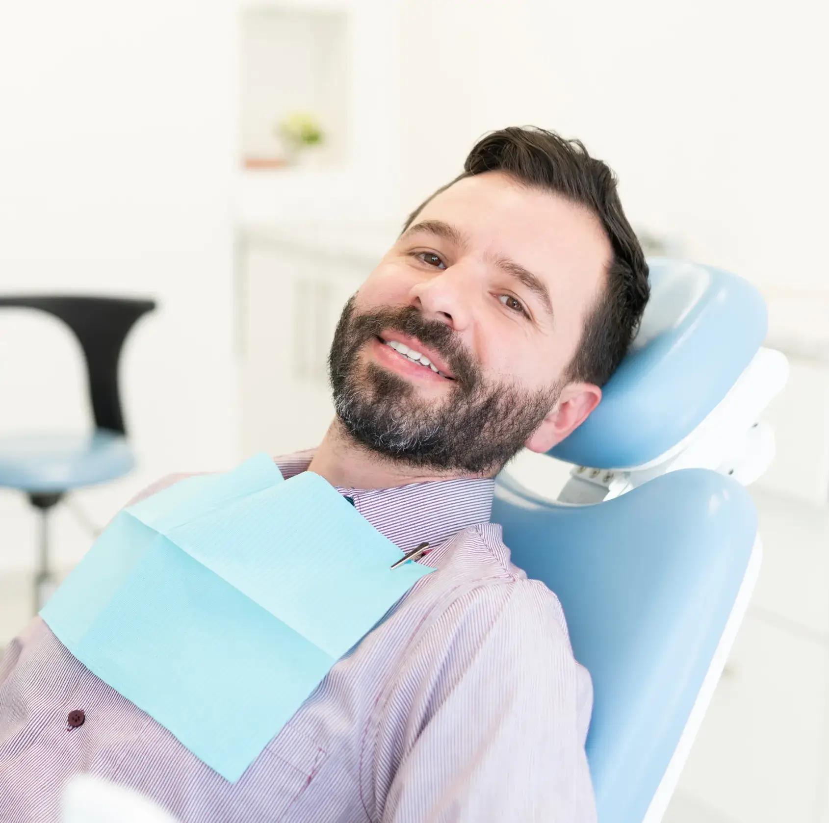 A man smiles while sitting in a dentist's chair, wearing a dental bib.