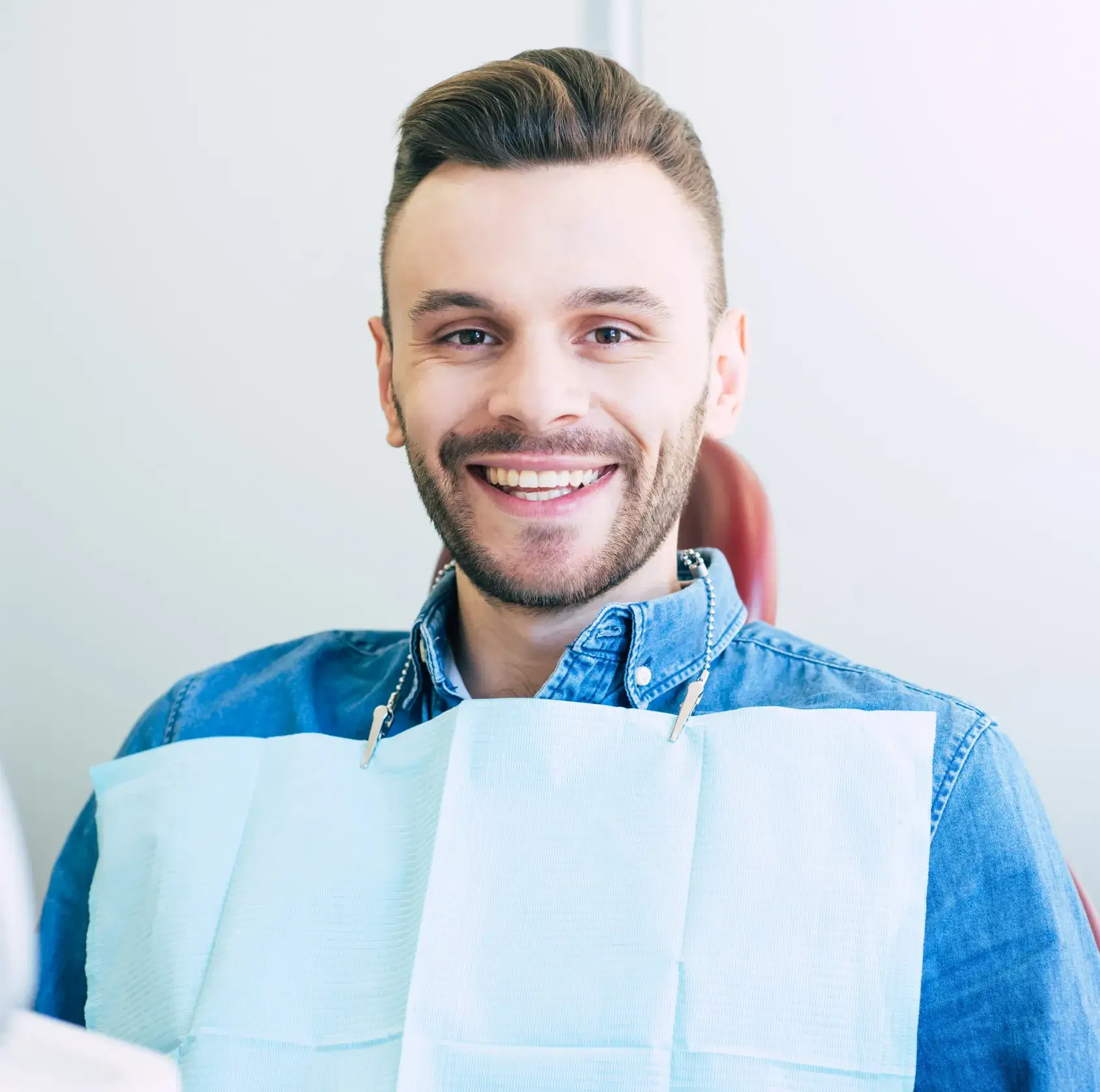 Man in a dental chair smiling with a dental bib on.
