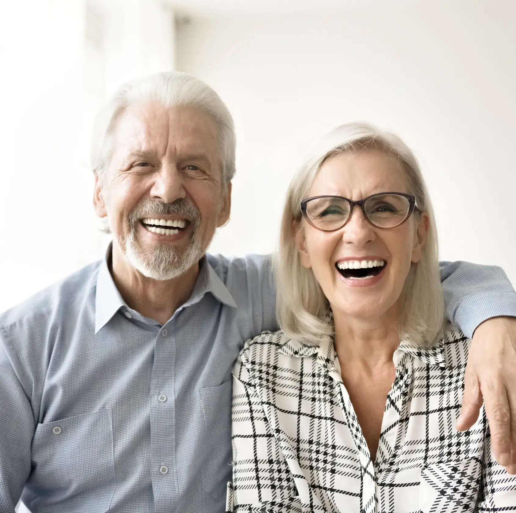 An older couple smiling, sitting close together, with the man's arm around the woman's shoulder.