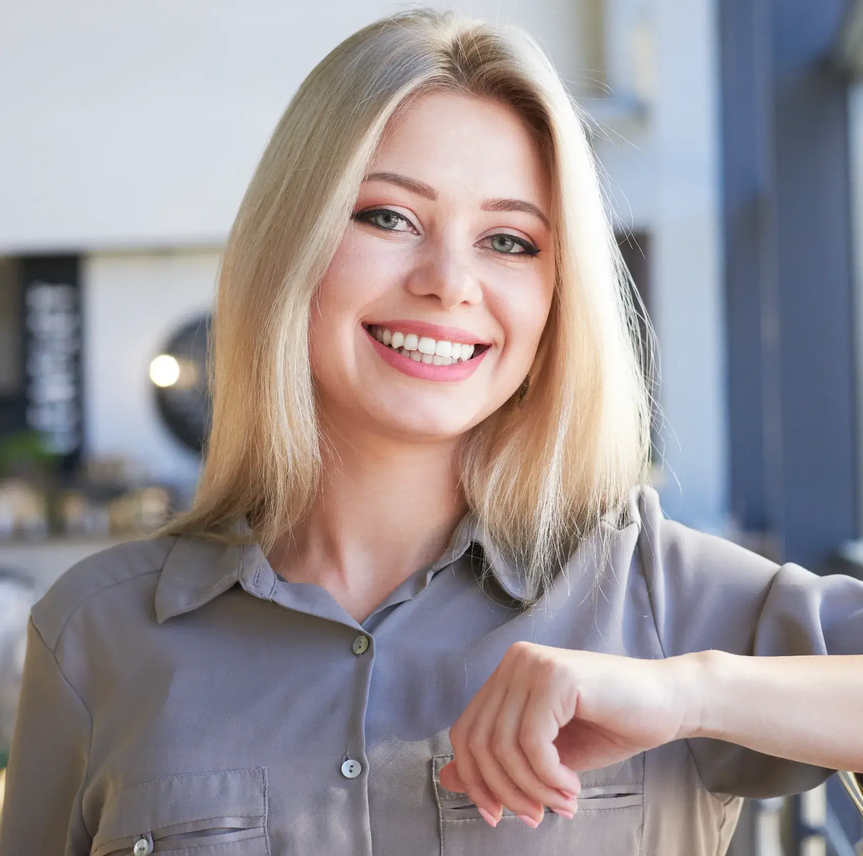 Smiling woman with long blond hair wearing a gray shirt, resting a hand on her arm.