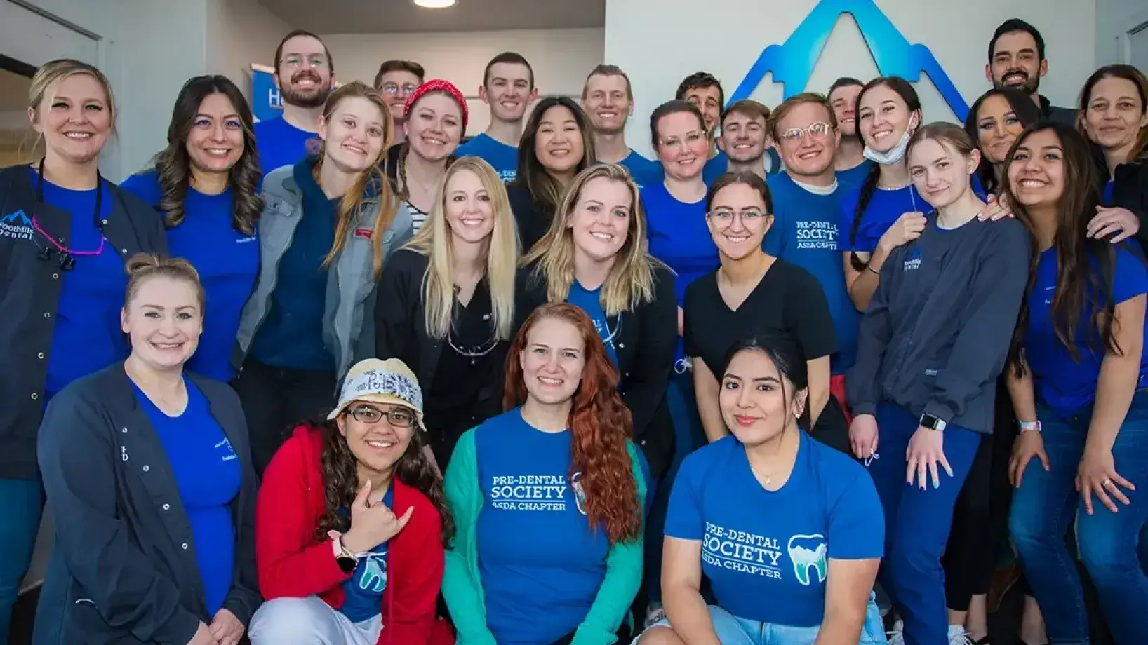 A group of smiling people wearing matching blue shirts poses together inside a building.