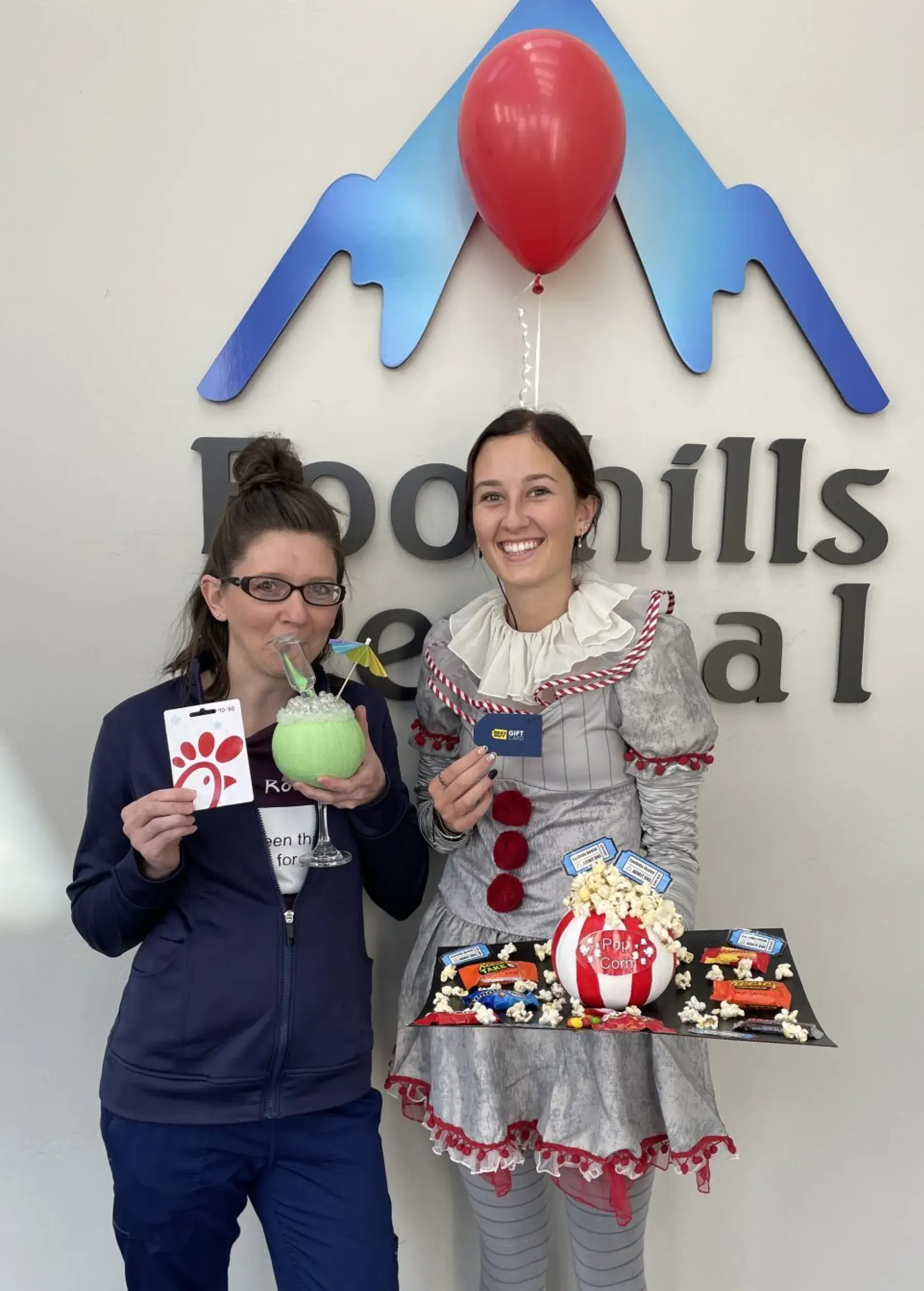 Two women smiling, one holding a drink and gift card, the other in a clown costume with treats.
