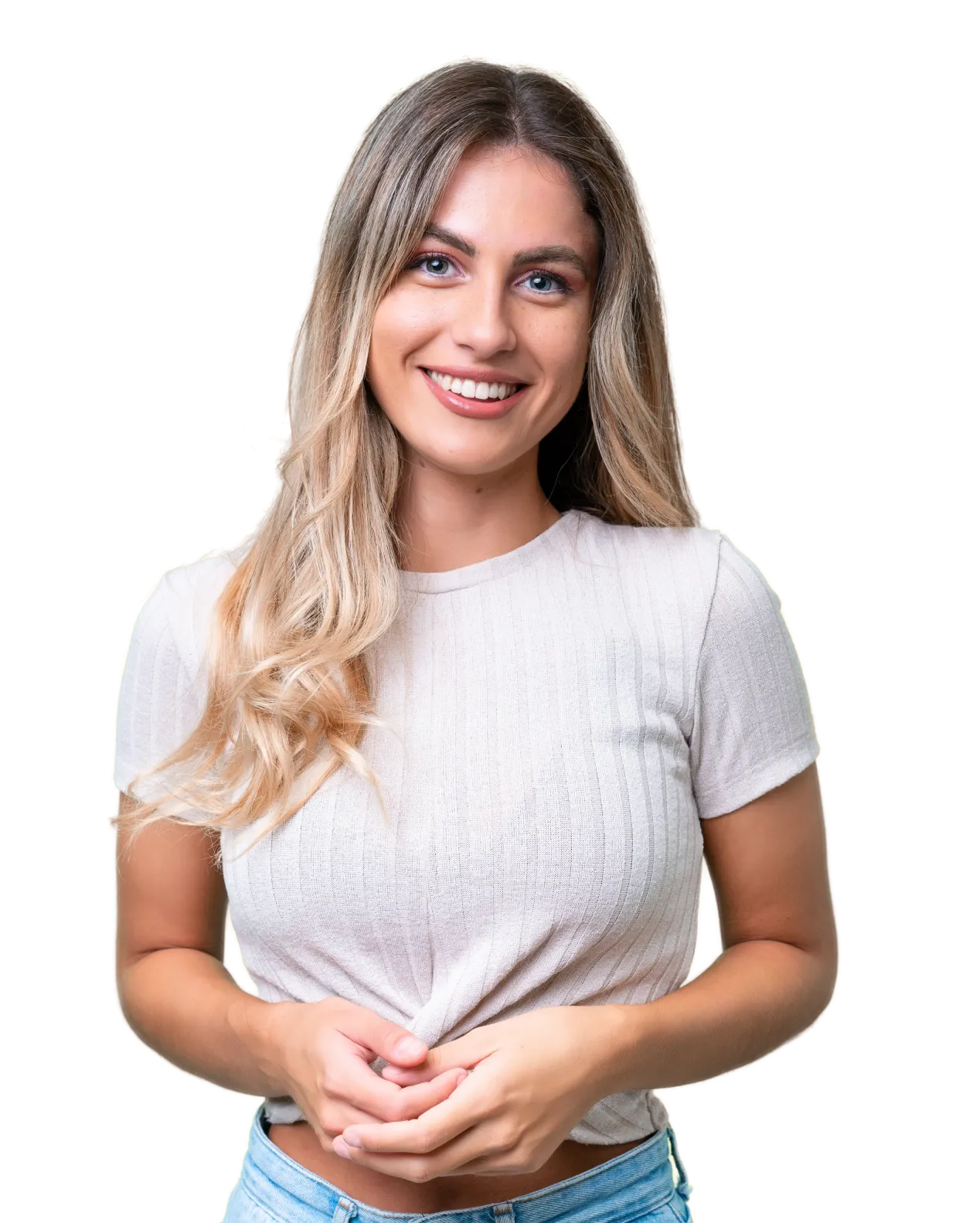 A person with long hair smiles, wearing a light-colored shirt and holding their hands together.