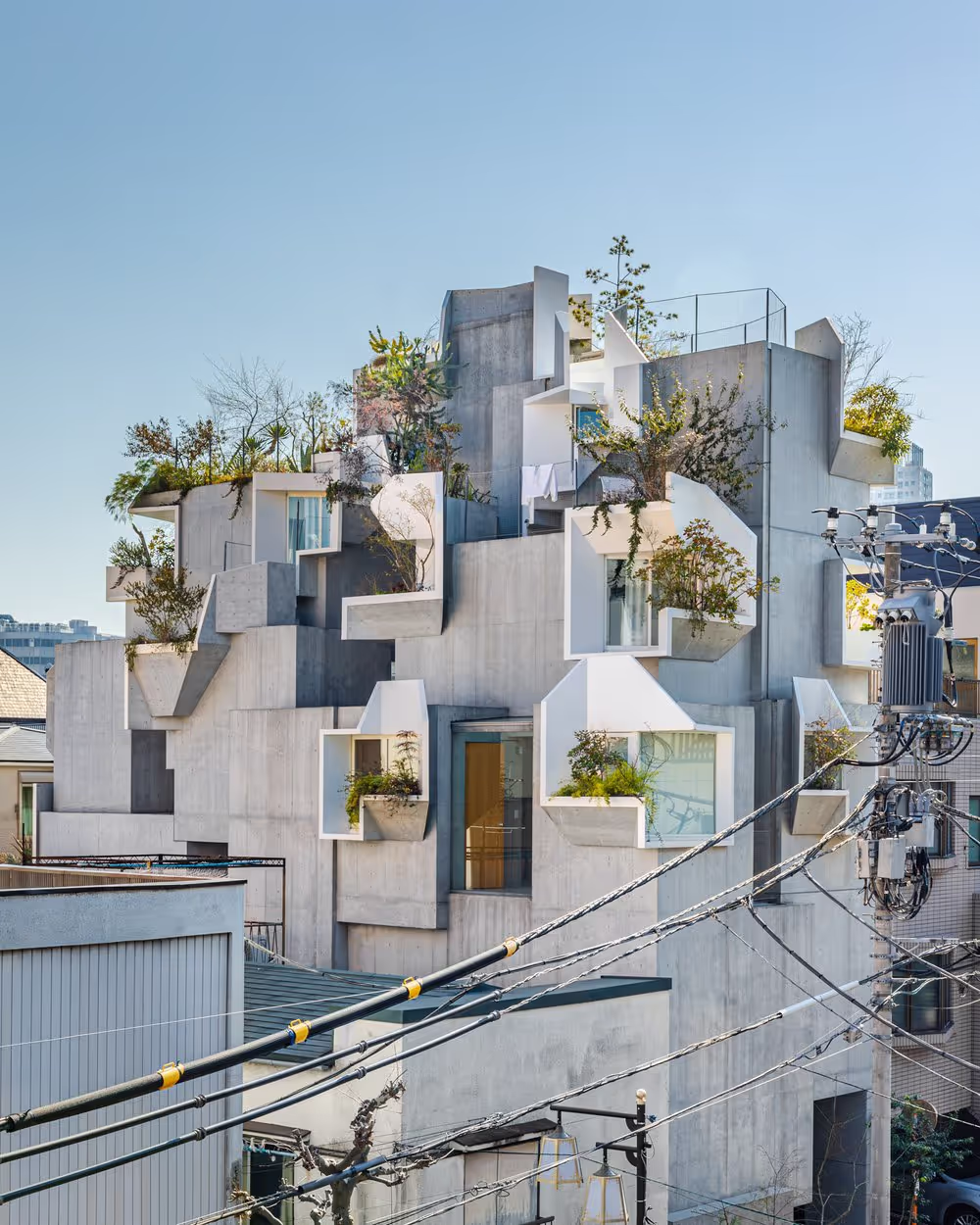Modern concrete building in Tokyo with geometric balconies filled with greenery, blending contemporary architecture with nature.