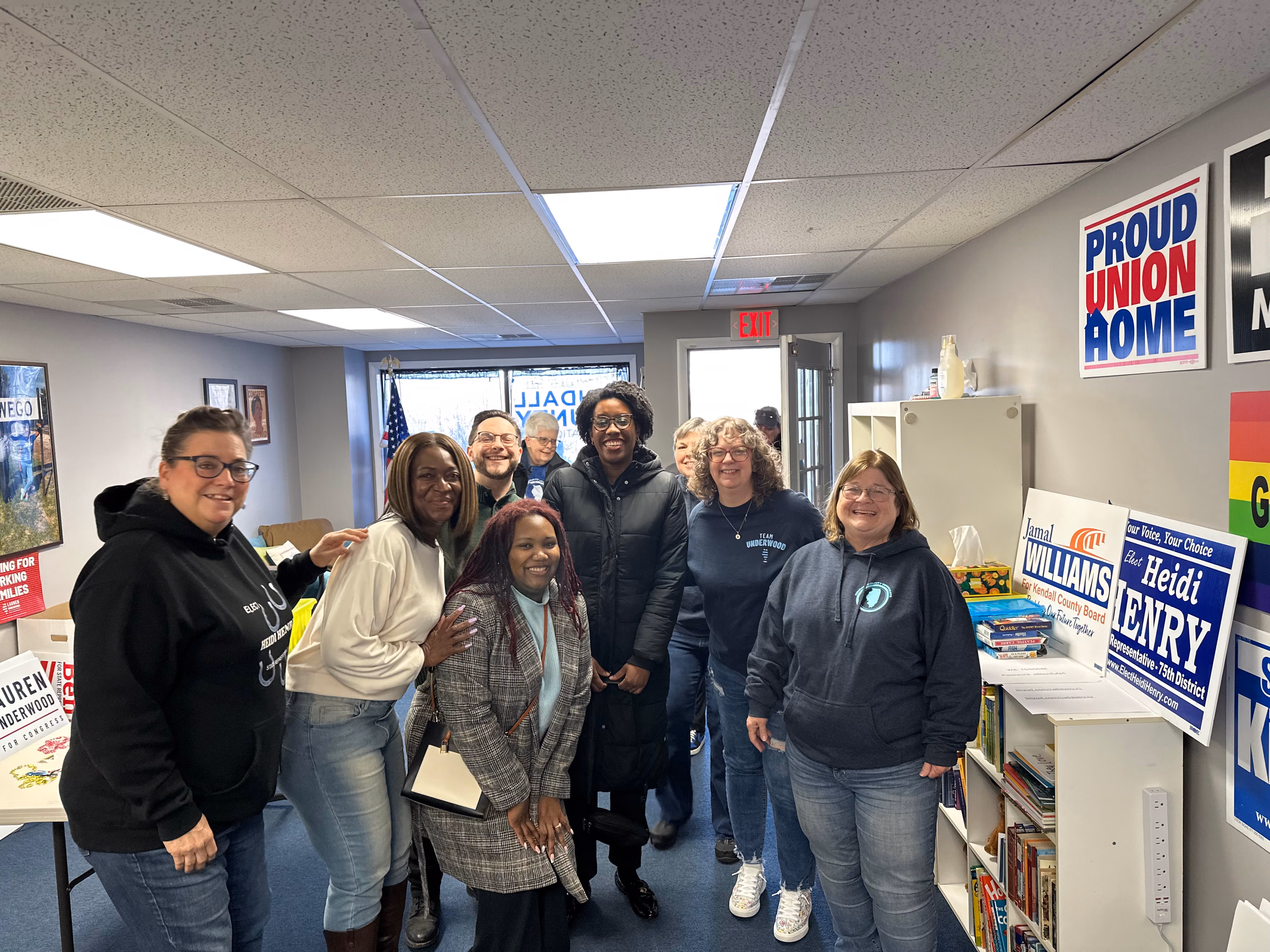 10 people pose for a photo in an office lined with political campaign signs. 