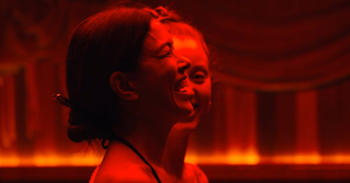 Two guests laughing together under red theatrical lighting at an Othership celebration event