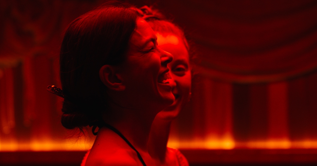 Two guests laughing together under red theatrical lighting at an Othership celebration event