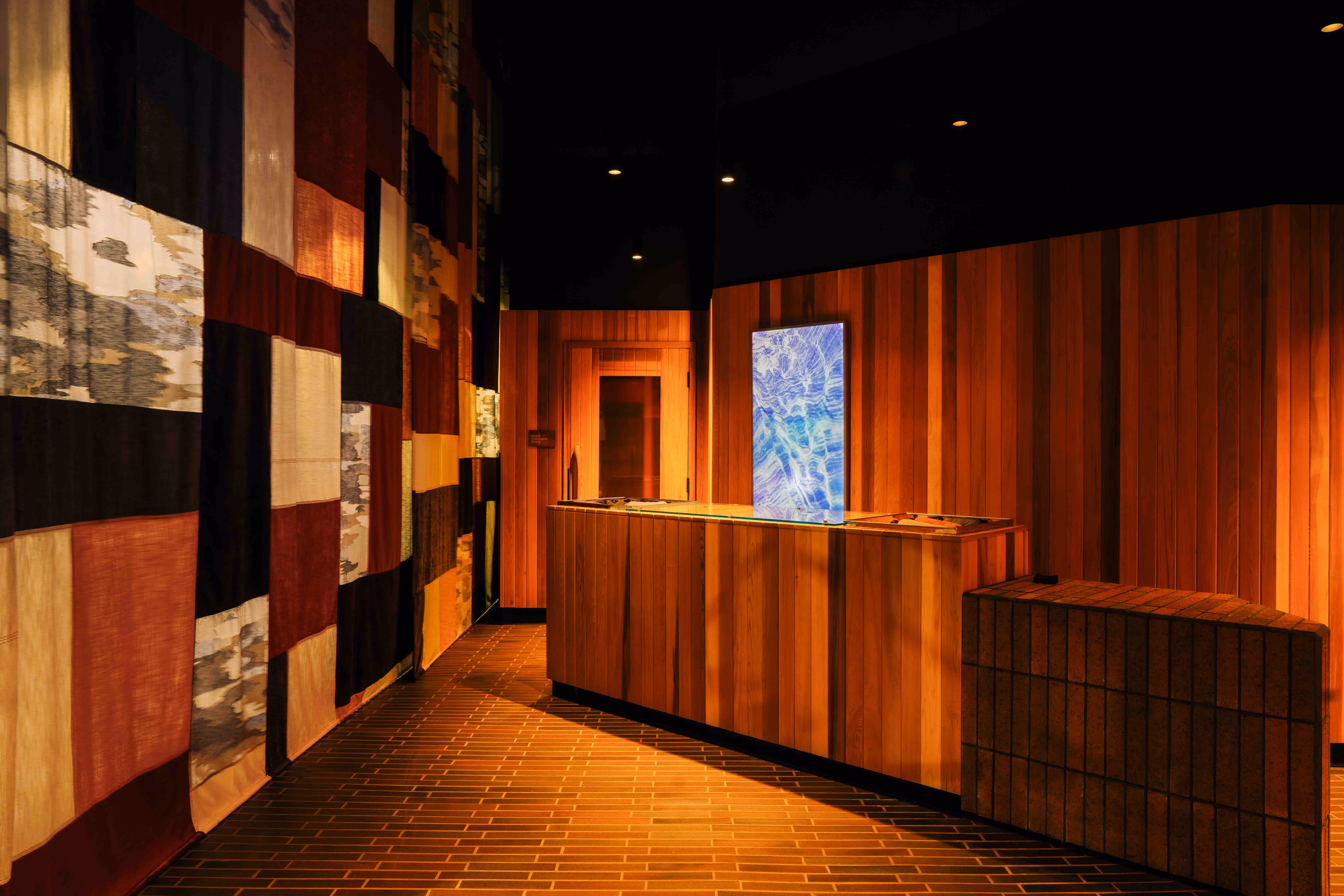 Warm-toned wooden reception desk with a blue abstract painting in a dimly lit hallway with patchwork wall art.