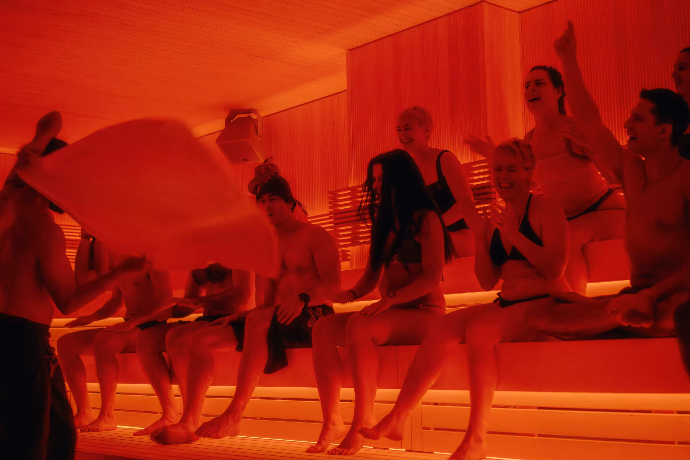 Group of people in swimwear relaxing and socializing in a warmly lit wooden sauna.