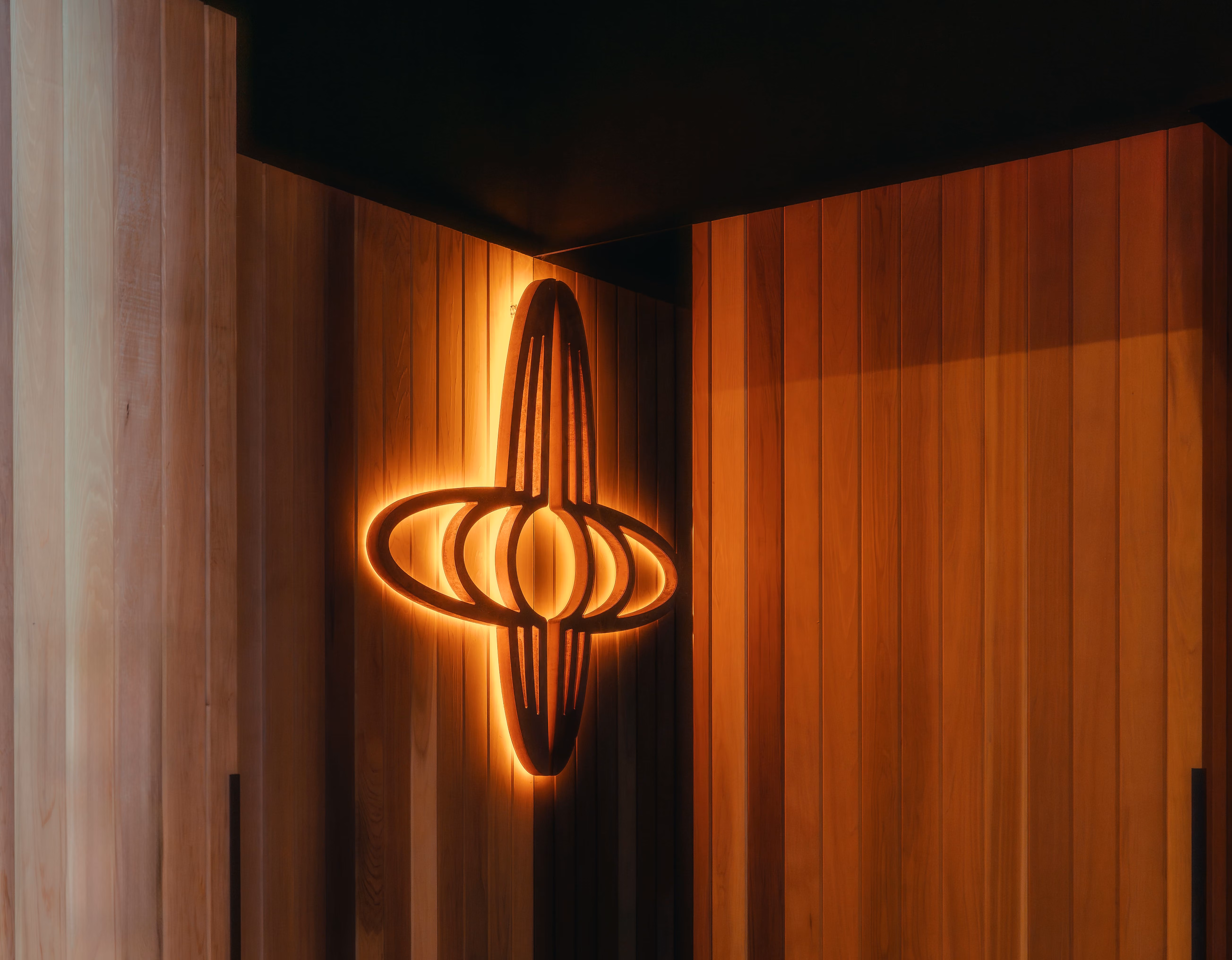 Glowing modern wall light with vertical and horizontal oval design on wooden panel walls.